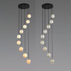 Two Clérachic sphere pendants side by side on grey, the spheres stepping down in a spiral, one warm in tone and one pale.