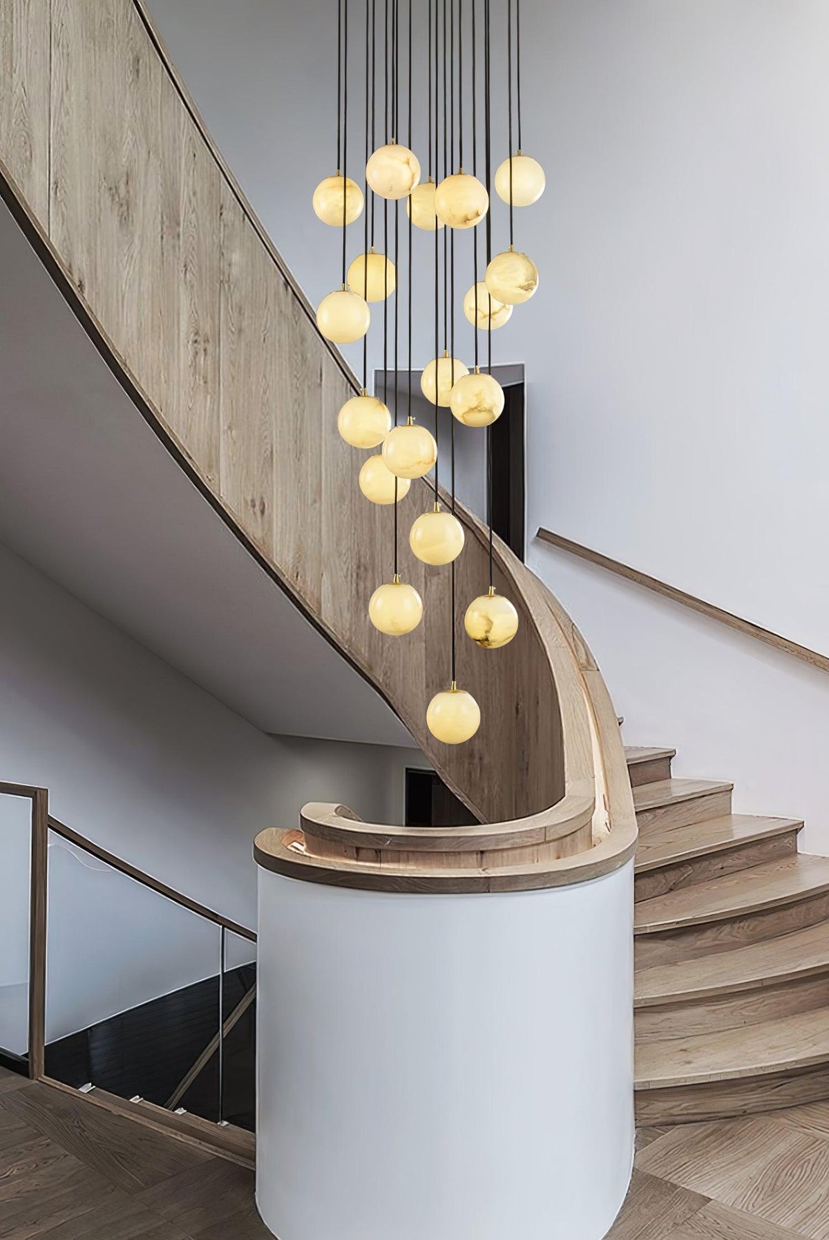 Clérachic alabaster spheres fall in a column beside a curved pale oak stair and a white round wall.