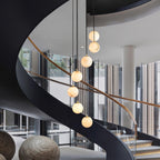 Clérachic alabaster spheres hang in a glass-walled atrium, beside the black curve of a spiral stair and large woven stone seats.