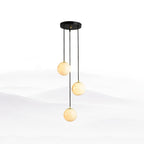 Three Clérachic alabaster spheres hanging from a small round black canopy, set against a soft white mountain-mist backdrop.