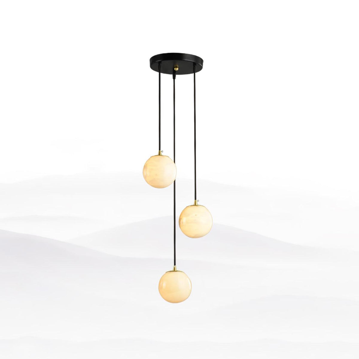Three Clérachic alabaster spheres hanging from a small round black canopy, set against a soft white mountain-mist backdrop.
