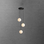 Three Clérachic alabaster spheres on black cords, hanging from a round canopy against a dark concrete-effect wall.