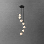 Eight Clérachic alabaster spheres hang in a loose spiral from a black canopy, in front of a grey concrete-effect wall.