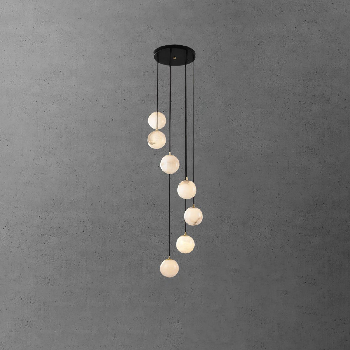 Eight Clérachic alabaster spheres hang in a loose spiral from a black canopy, in front of a grey concrete-effect wall.