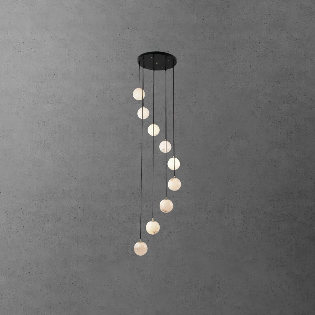 Long Clérachic alabaster sphere spiral, slim and tall, hanging from a round black canopy on a grey textured wall.
