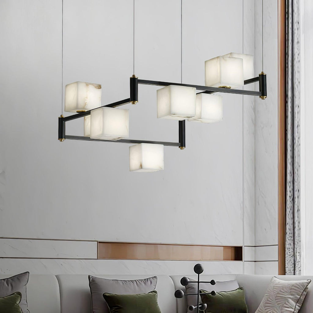 Clérachic box chandelier lit against a pale marble wall above a sofa with green cushions.
