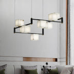 Clérachic box chandelier lit against a pale marble wall above a sofa with green cushions.