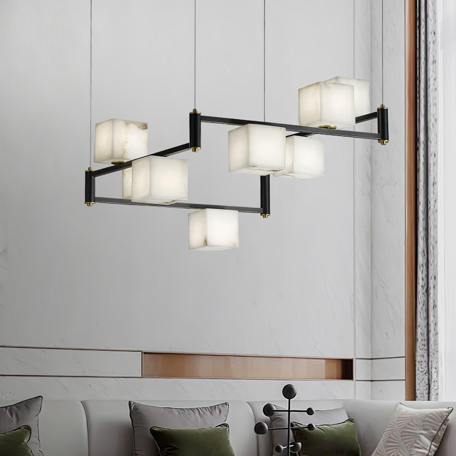 Clérachic box chandelier lit against a pale marble wall above a sofa with green cushions.