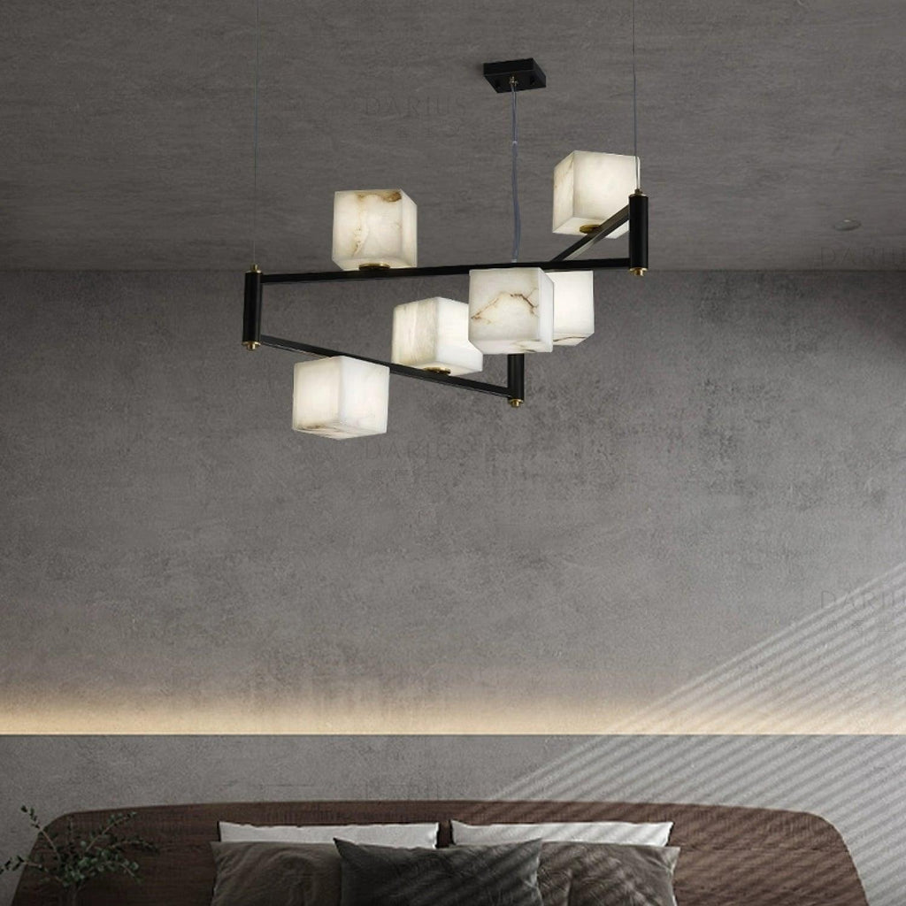 The Clérachic box chandelier lit over a bed in a concrete-walled room with a cove-lit ledge.