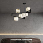 The Clérachic box chandelier lit over a bed in a concrete-walled room with a cove-lit ledge.