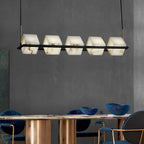 The linear Clérachic box chandelier lit above a marble dining table with blue velvet chairs.