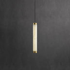 Clérachic alabaster pendant hanging as a slim lit column with brushed brass caps against a dark grey plaster wall.