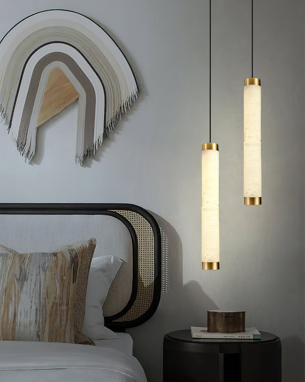 The Clérachic pendants flanking a caned bed, their alabaster columns echoing the warmth of the woven wall hanging.