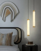 The Clérachic pendants flanking a caned bed, their alabaster columns echoing the warmth of the woven wall hanging.
