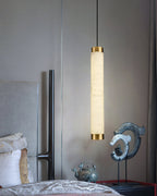 Clérachic pendant dropped beside an upholstered bed, its lit alabaster column framed by a dark bedroom corner.
