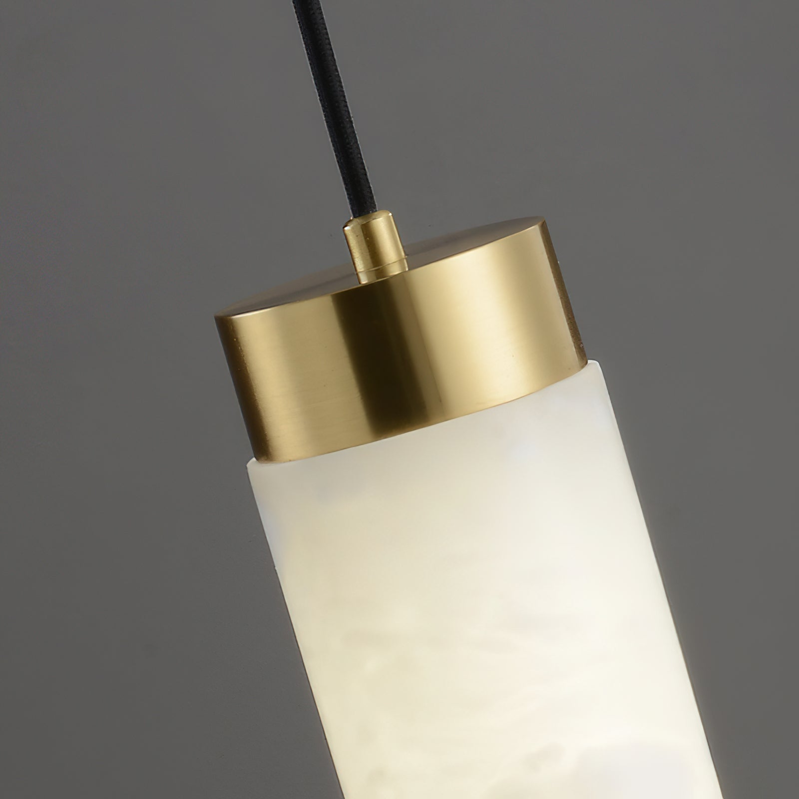 Clérachic pendant close up at the brushed brass top cap, where the black cable meets the alabaster tube.