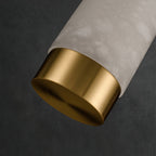The Clérachic pendant's brushed brass base cap shown at an angle beside the softly glowing alabaster tube.