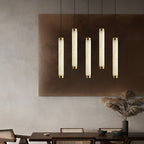 Clérachic pendants hung in a row of five in front of a bronze wall panel above a long dining table.