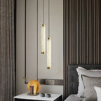 The Clérachic pendants dropped at two lengths beside a bed, glowing against dark fluted wood panelling.