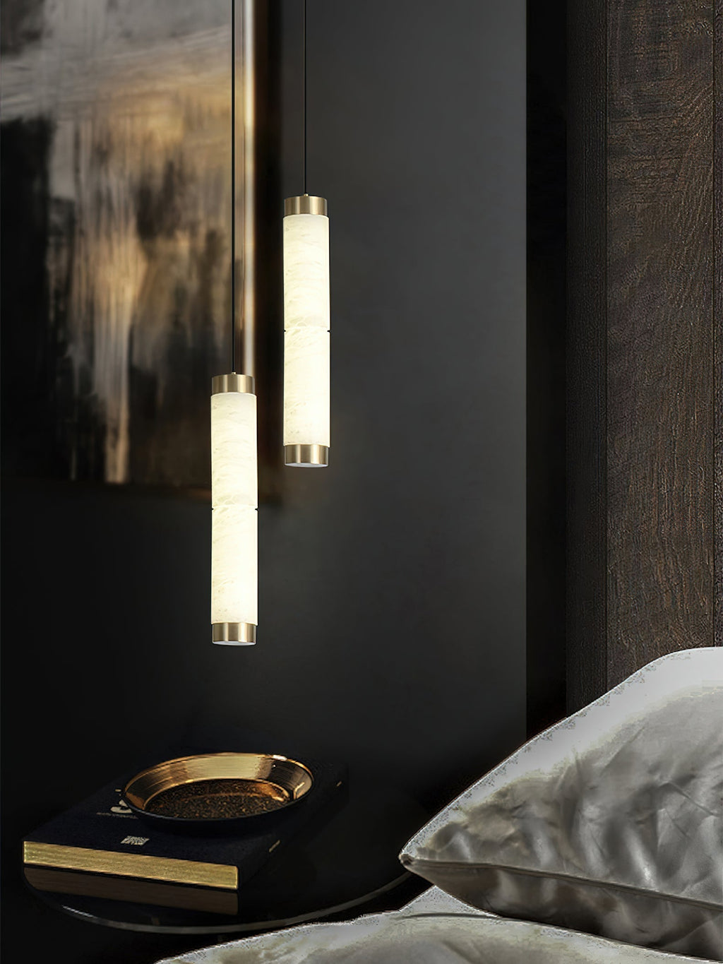 Clérachic pendants over a bedside table, warm alabaster light falling on a brass dish and stacked books.