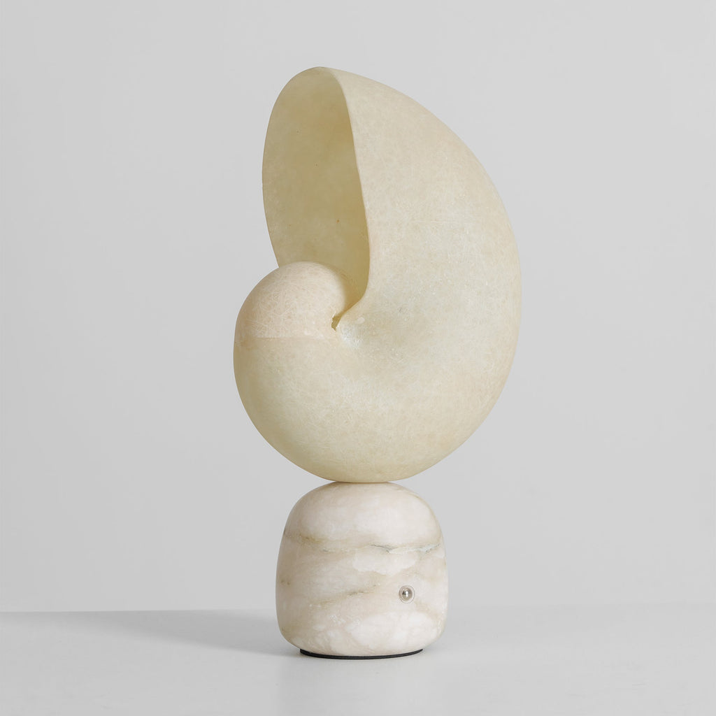 Unlit Clérachic alabaster conch lamp with a veined stone base and a small metal touch point, against a pale grey backdrop.