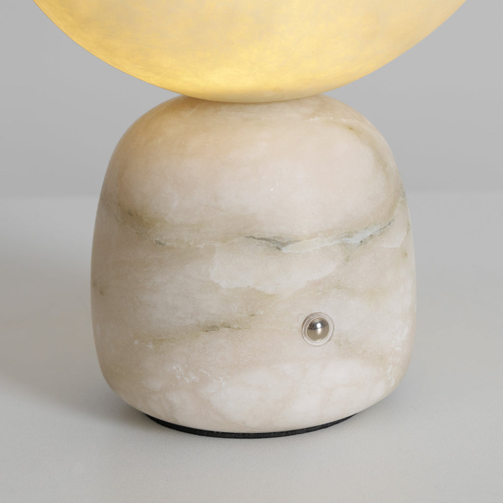 Close view of the veined white stone base on this Clérachic lamp, with its small metal touch point and the glowing shade above.