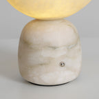 Close view of the veined white stone base on this Clérachic lamp, with its small metal touch point and the glowing shade above.