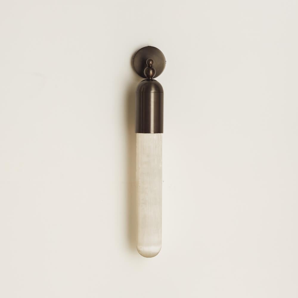 Clérachic Alabaster Tube Wall Sconce in black on a cream wall, unlit, with the grain of the natural alabaster tube visible.
