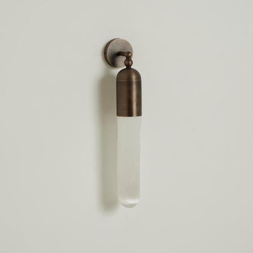 Antique brass Clérachic Alabaster Tube Wall Sconce on a soft grey wall, three-quarter view with its long shadow beside it.