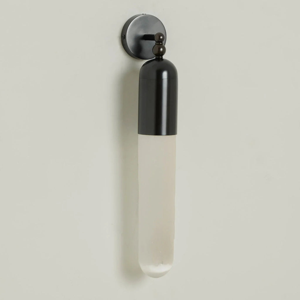 Clérachic Alabaster Tube Wall Sconce in black hung on a pale wall, full length shown from cap to the rounded stone tip.