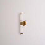 Unlit veined white tubes with gold end caps and a round gold plate, this Clérachic wall light on a plain pale grey wall.