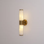 Lit Clérachic wall light on a grey wall, with warm light glowing through both veined white tubes and a gold band between them.
