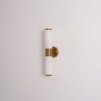 Unlit Clérachic wall light on a pale wall, with veined white tubes, a gold band and a round gold plate seen from a slight angle.