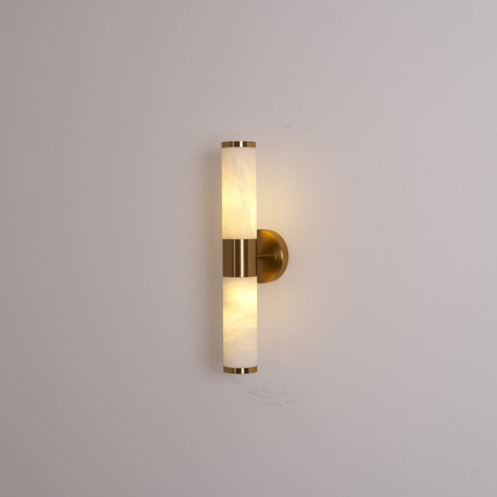 Lit Clérachic wall light on a grey wall, with warm light inside the veined tubes and a gold collar and wall plate.