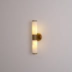 Lit Clérachic wall light on a grey wall, with warm light inside the veined tubes and a gold collar and wall plate.