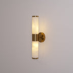 A Clérachic wall light glowing evenly in both veined white tubes against a soft grey wall, with a gold collar at the centre.