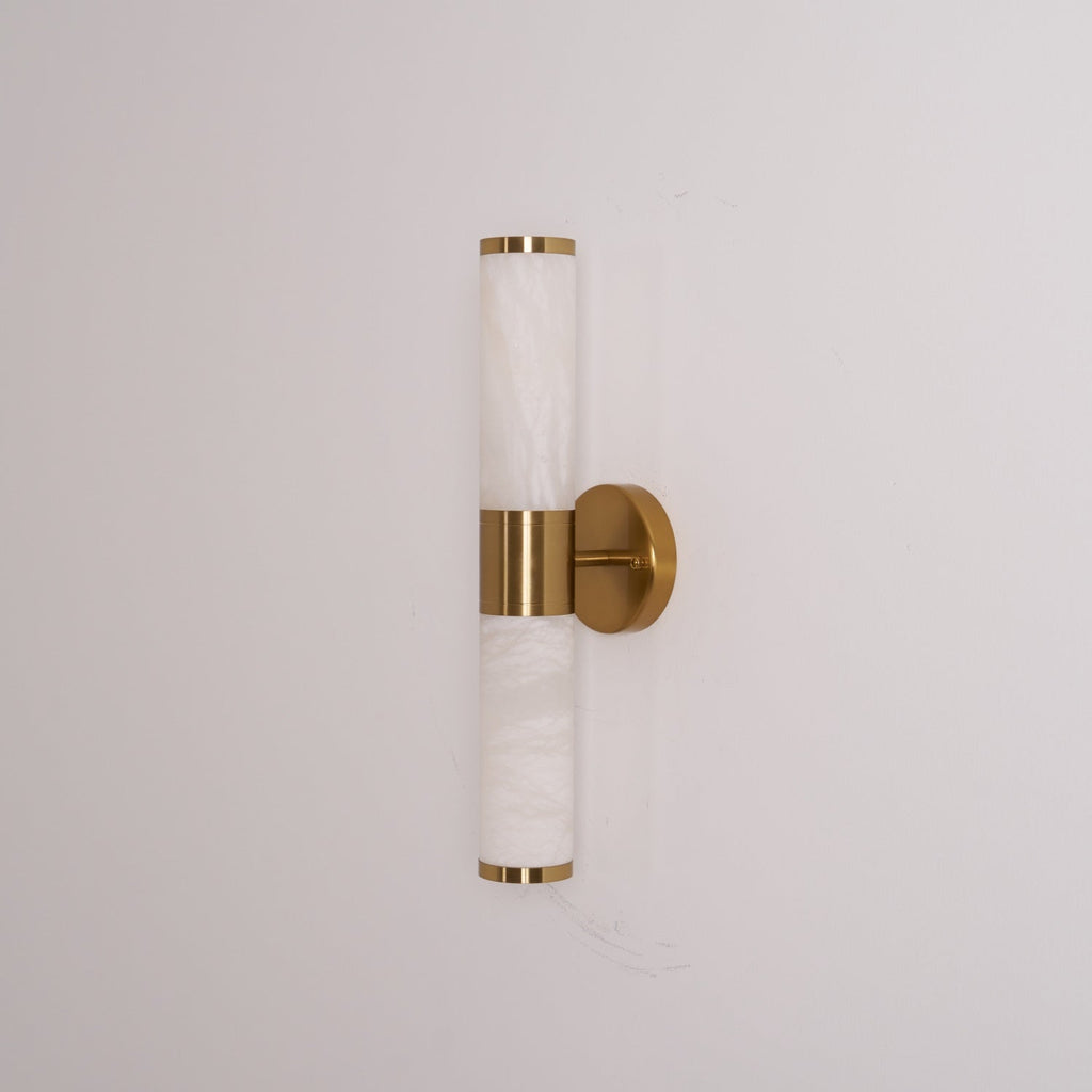 This Clérachic wall light switched off, with pale veined tubes, gold rims and a round gold plate on a light grey wall.