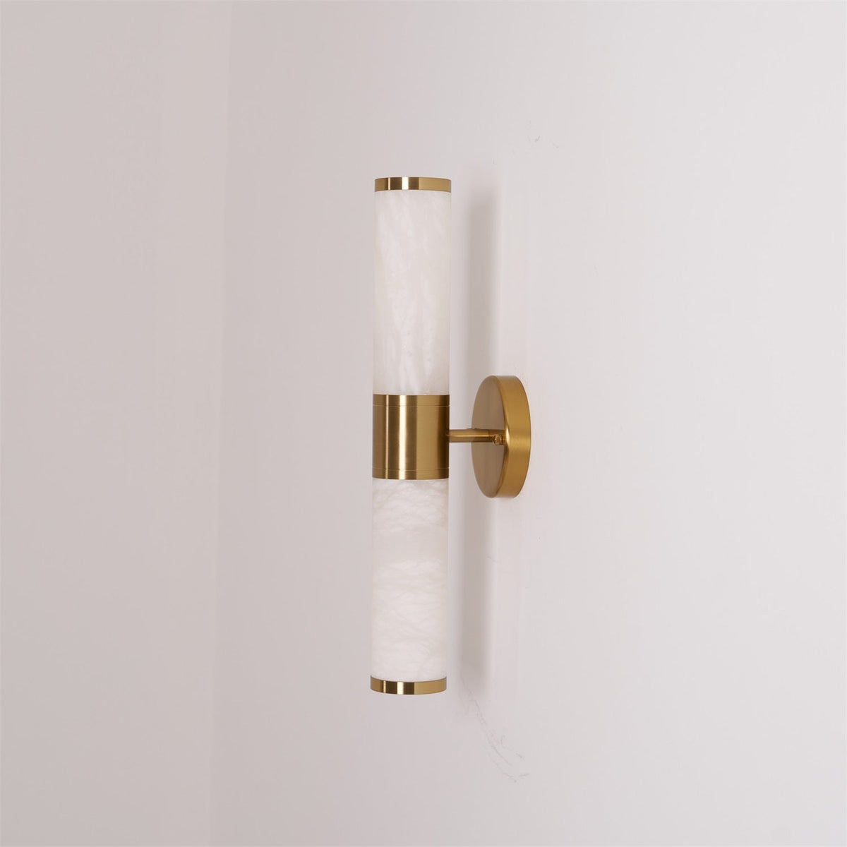 Angled view of the unlit Clérachic wall light, with white veined tubes and a gold band against a pale wall with a corner edge.