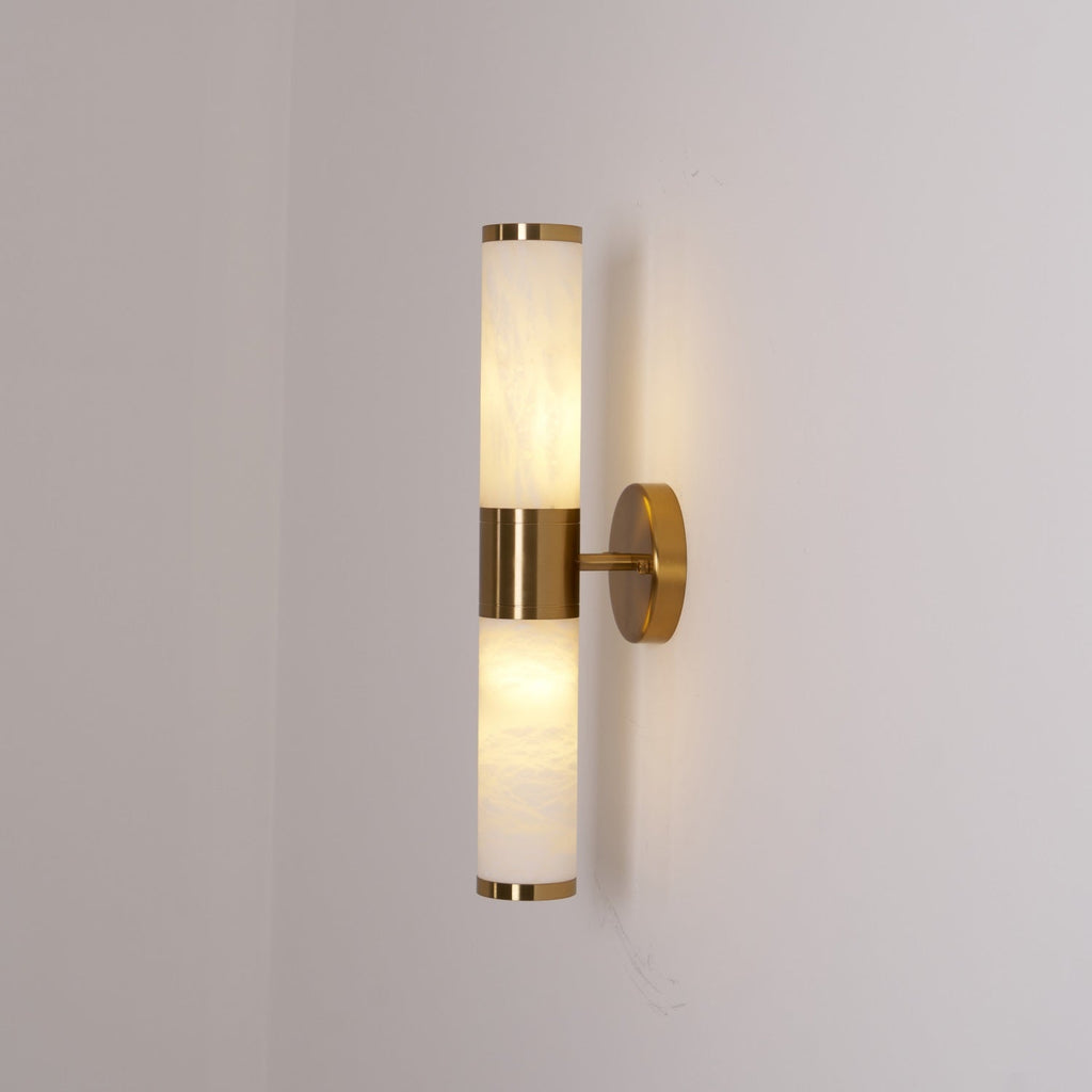 Clérachic wall light lit in a corner of a grey room, with both veined tubes glowing and a gold band holding them together.