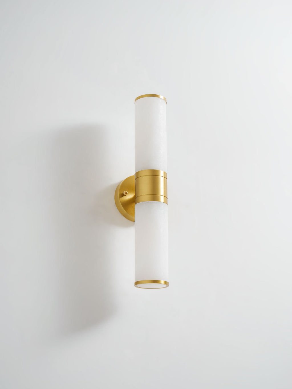 Clérachic wall light with frosted white tubes and a brushed gold band and plate on a white wall, photographed from slightly above.