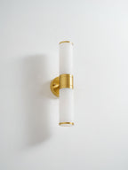 Clérachic wall light with frosted white tubes and a brushed gold band and plate on a white wall, photographed from slightly above.