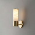 A single veined alabaster tube on a gold collar and short arm, a one-tube Clérachic wall light glowing warmly on a grey wall.