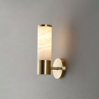 A single veined alabaster tube on a gold collar and short arm, a one-tube Clérachic wall light glowing warmly on a grey wall.