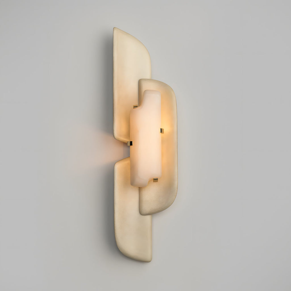 A lit Clérachic wall lamp on a pale grey wall, its alabaster glowing softly behind overlapping beige panels.