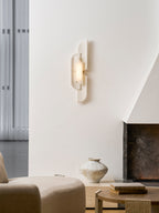 A Clérachic wall lamp hangs high on a white plaster wall beside a sheer curtain, over a cream chair and a fireplace.