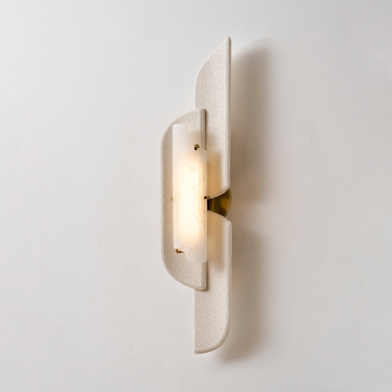 Close three-quarter view of a lit Clérachic wall lamp, its textured beige panels and glowing alabaster against a pale wall.