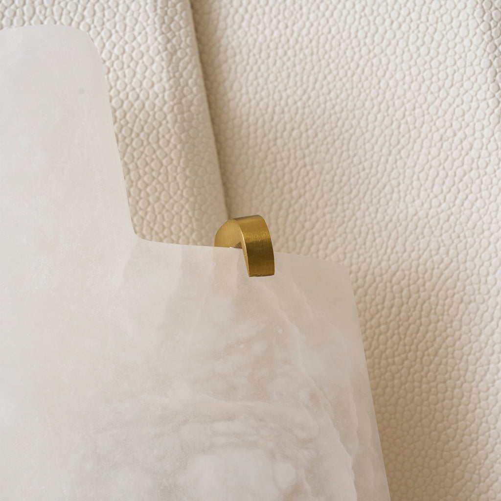 Close view of a brass clip holding the cloudy alabaster slab against the beige panel of this Clérachic wall lamp.