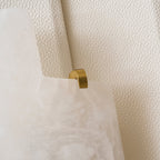 Close view of a brass clip holding the cloudy alabaster slab against the beige panel of this Clérachic wall lamp.