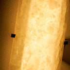 Close view of the alabaster on this Clérachic wall lamp lit from behind, glowing amber with cloudy veins.