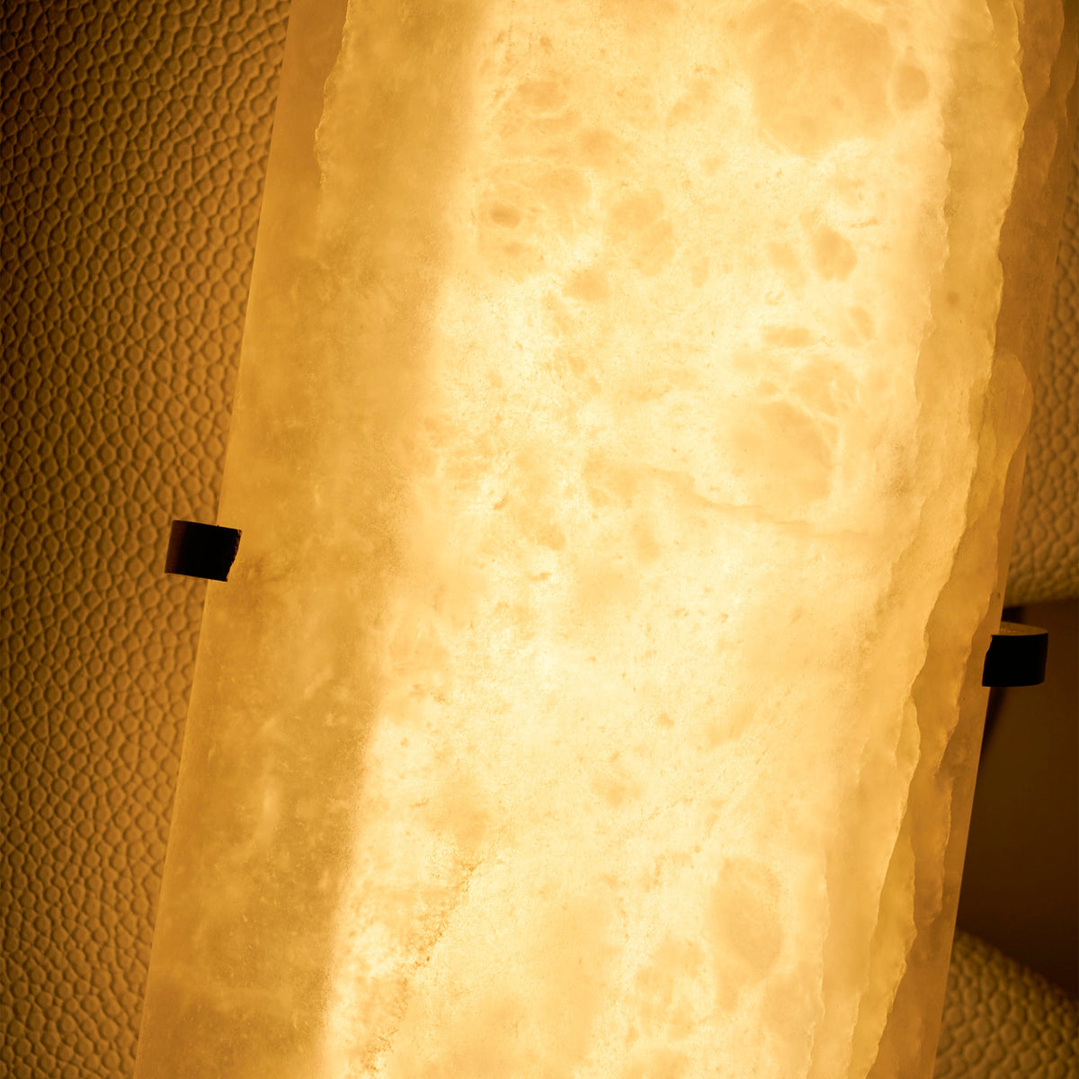Close view of the alabaster on this Clérachic wall lamp lit from behind, glowing amber with cloudy veins.